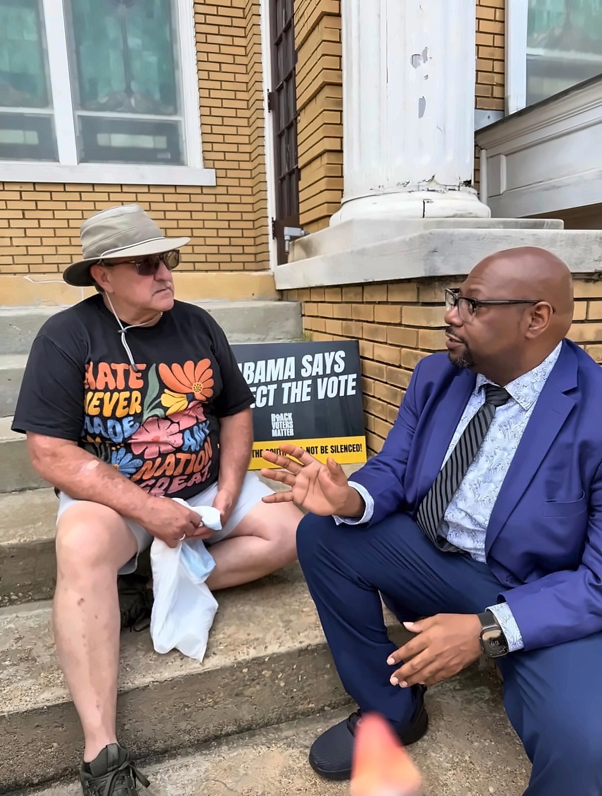 Kermit Williams talking with a man on church steps beside a Black Voters Matter sign
