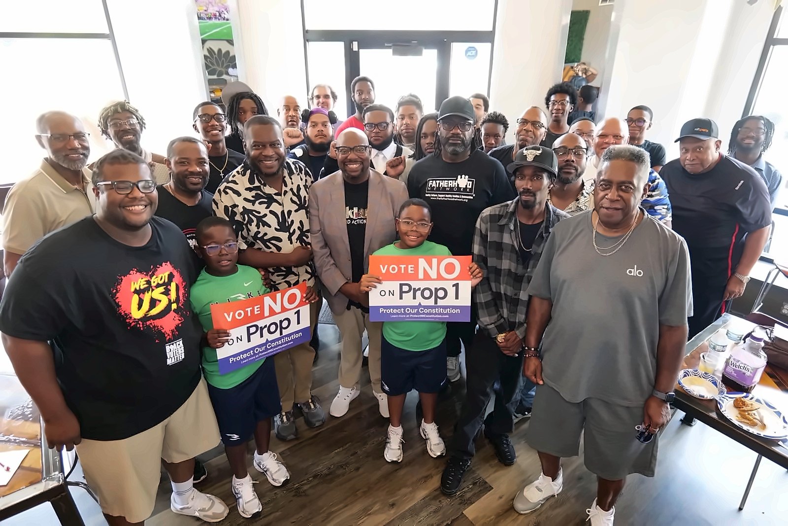 Kermit Williams with a large group of men and boys holding Vote No on Prop 1 signs
