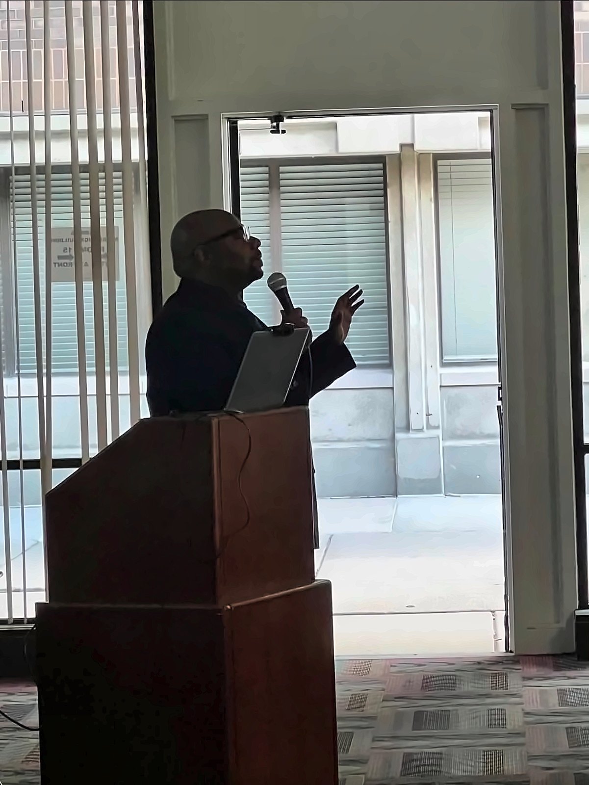 Silhouette of Kermit Williams speaking with a microphone at a podium