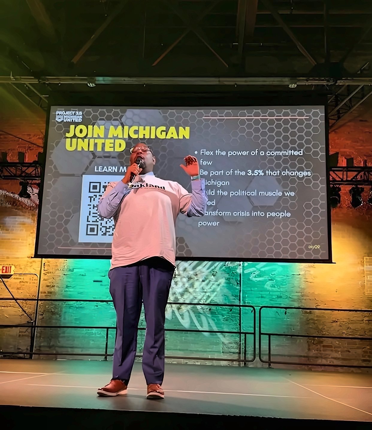 Kermit Williams speaking on stage in front of a Join Michigan United slide